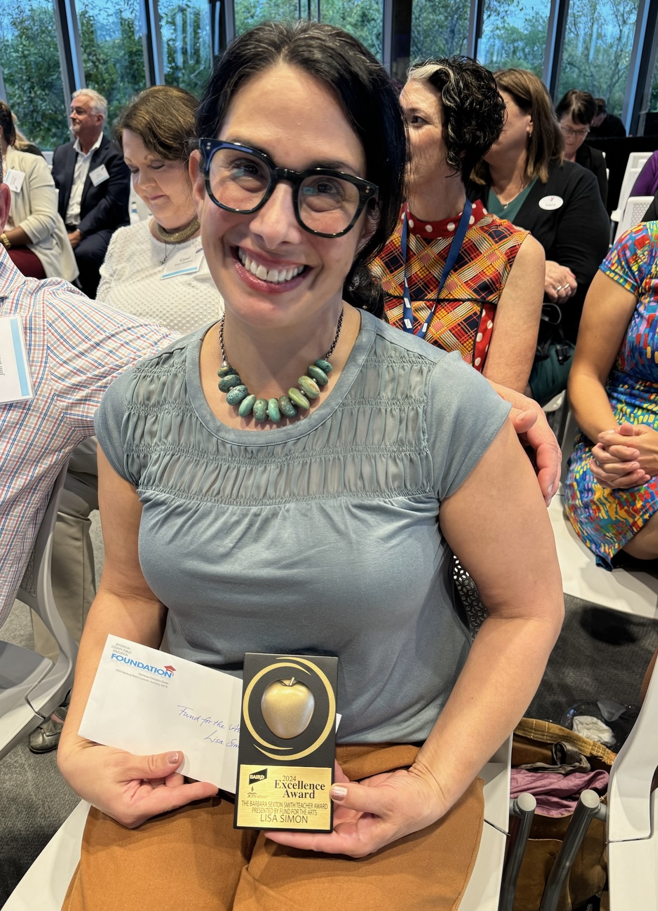 Lisa Simon smiling, wearing glasses and a turquoise beaded necklace