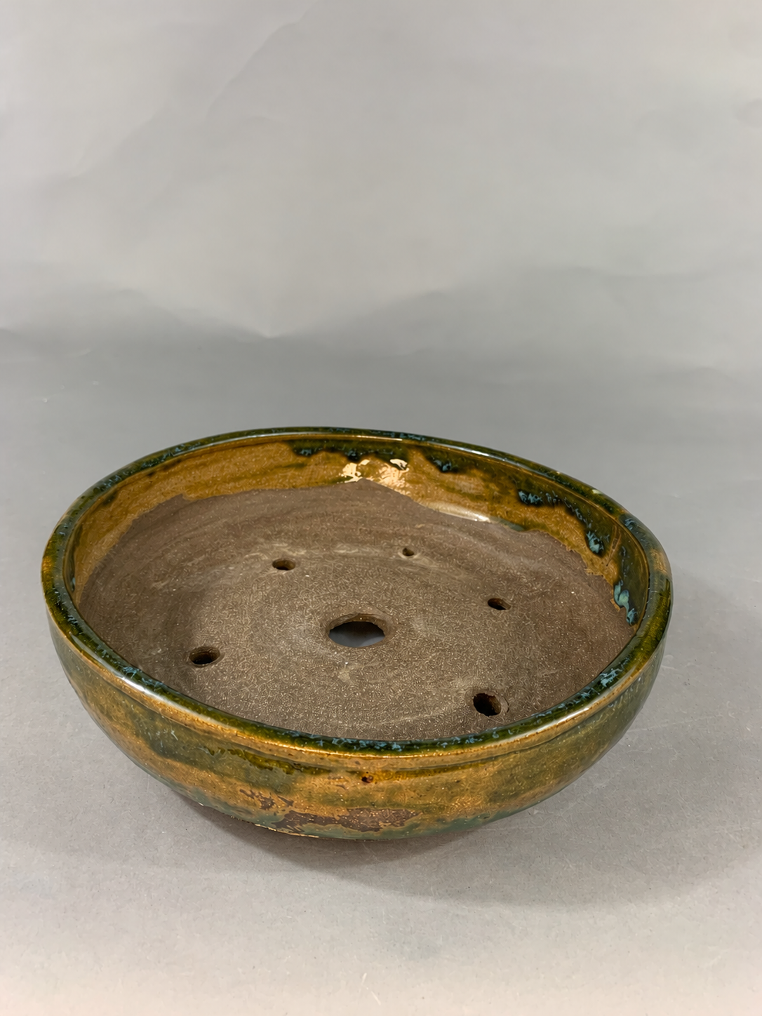 Shallow round pot with amber glaze, a green rim and visible drainage holes