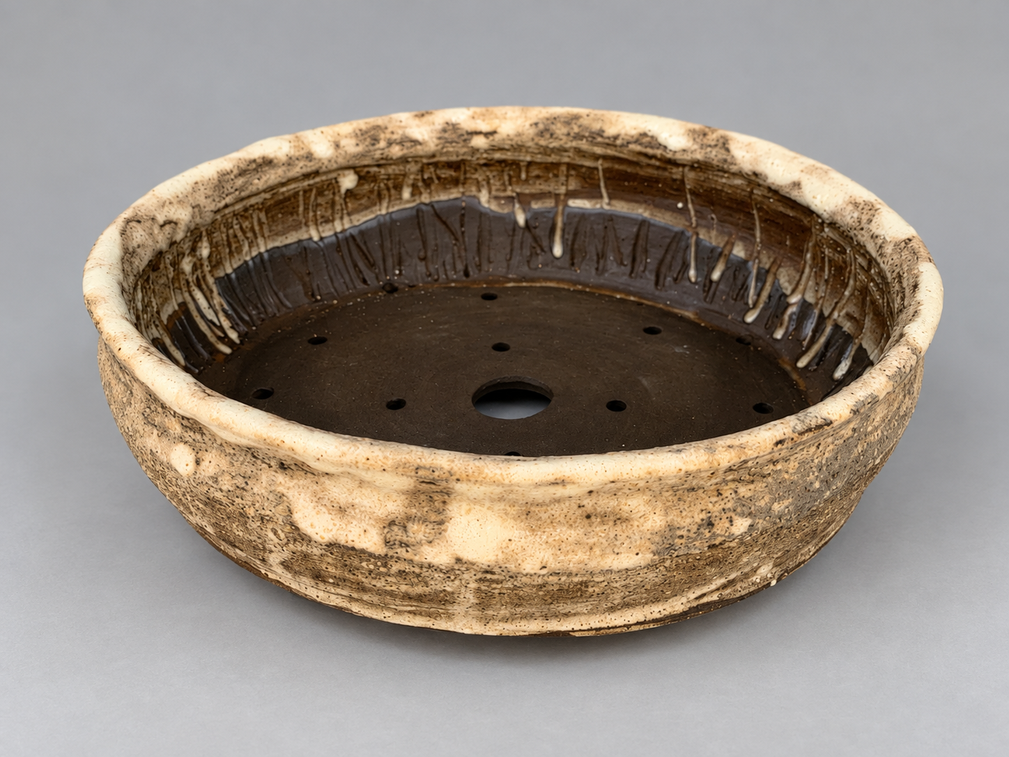 Broad round cream and brown mottled pot with visible drainage and wiring holes