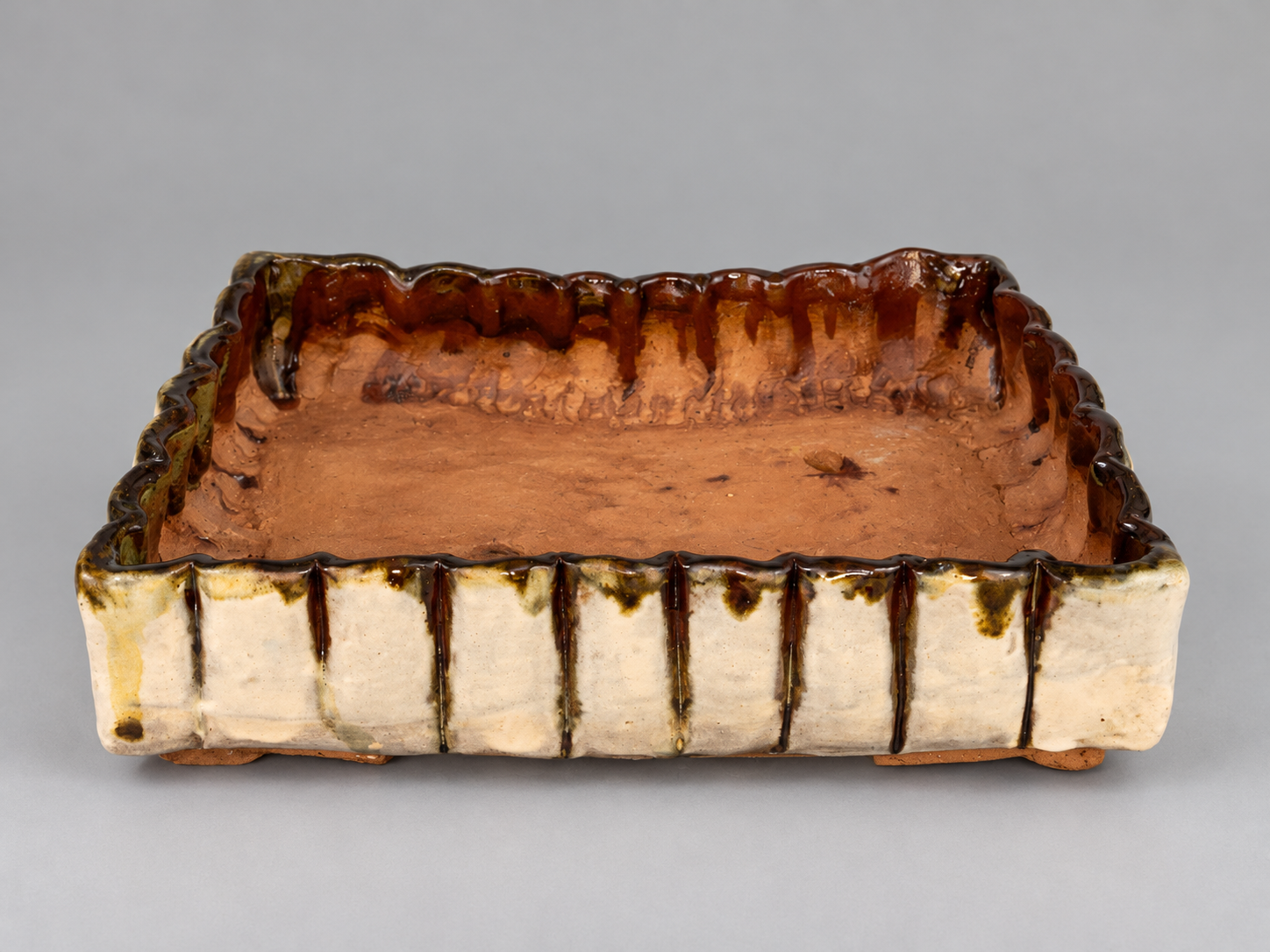 Rectangular cream and brown glazed pot with a fluted irregular rim and small feet