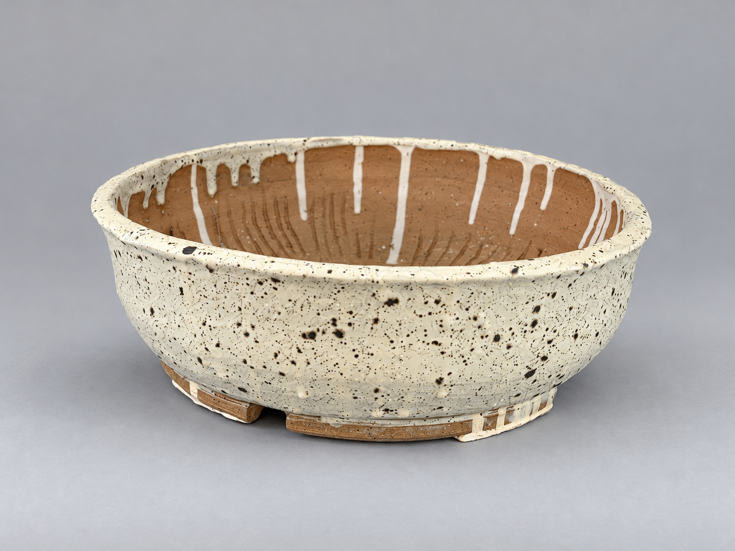Round cream-speckled glazed pot with an exposed clay interior and low feet