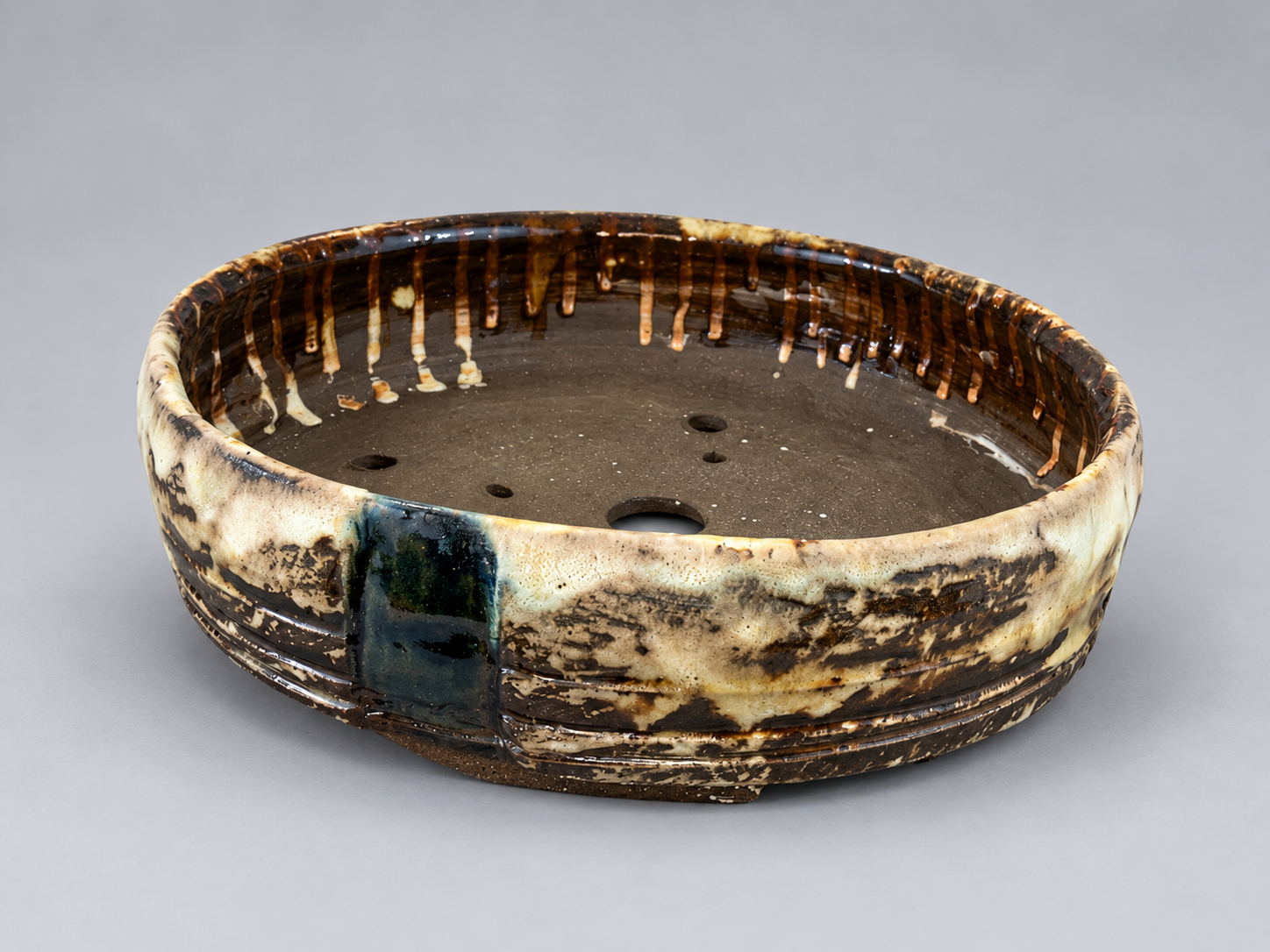 Round cream and brown glazed pot with a dark teal band and visible drainage holes