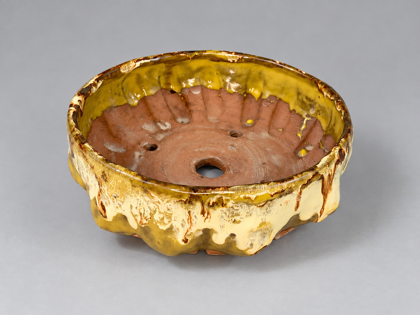 Golden yellow and cream glazed pot with an irregular scalloped rim and visible drainage hole