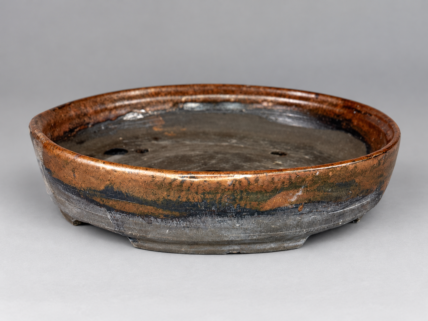 Shallow round rust and charcoal-glazed pot with a raised lip and low feet