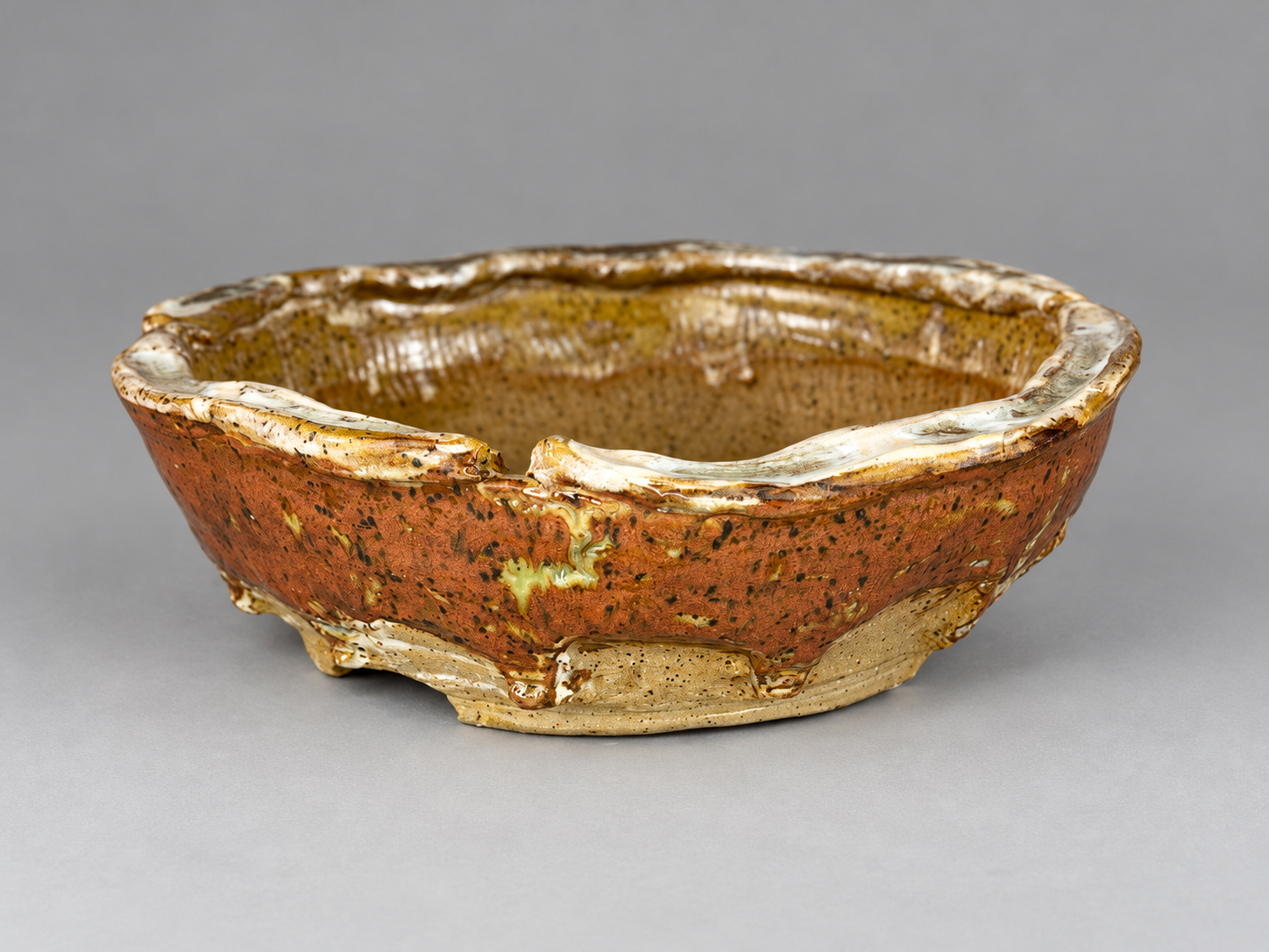 Rust-colored pot with a cream irregular rim, dark speckles and a low footed base
