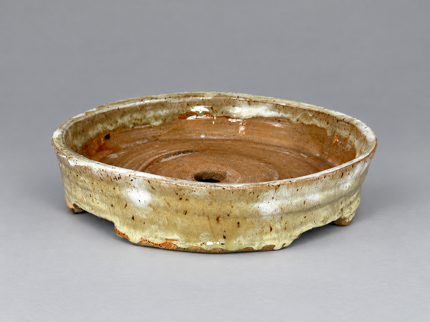 Low round cream-glazed pot with small feet and exposed clay inside