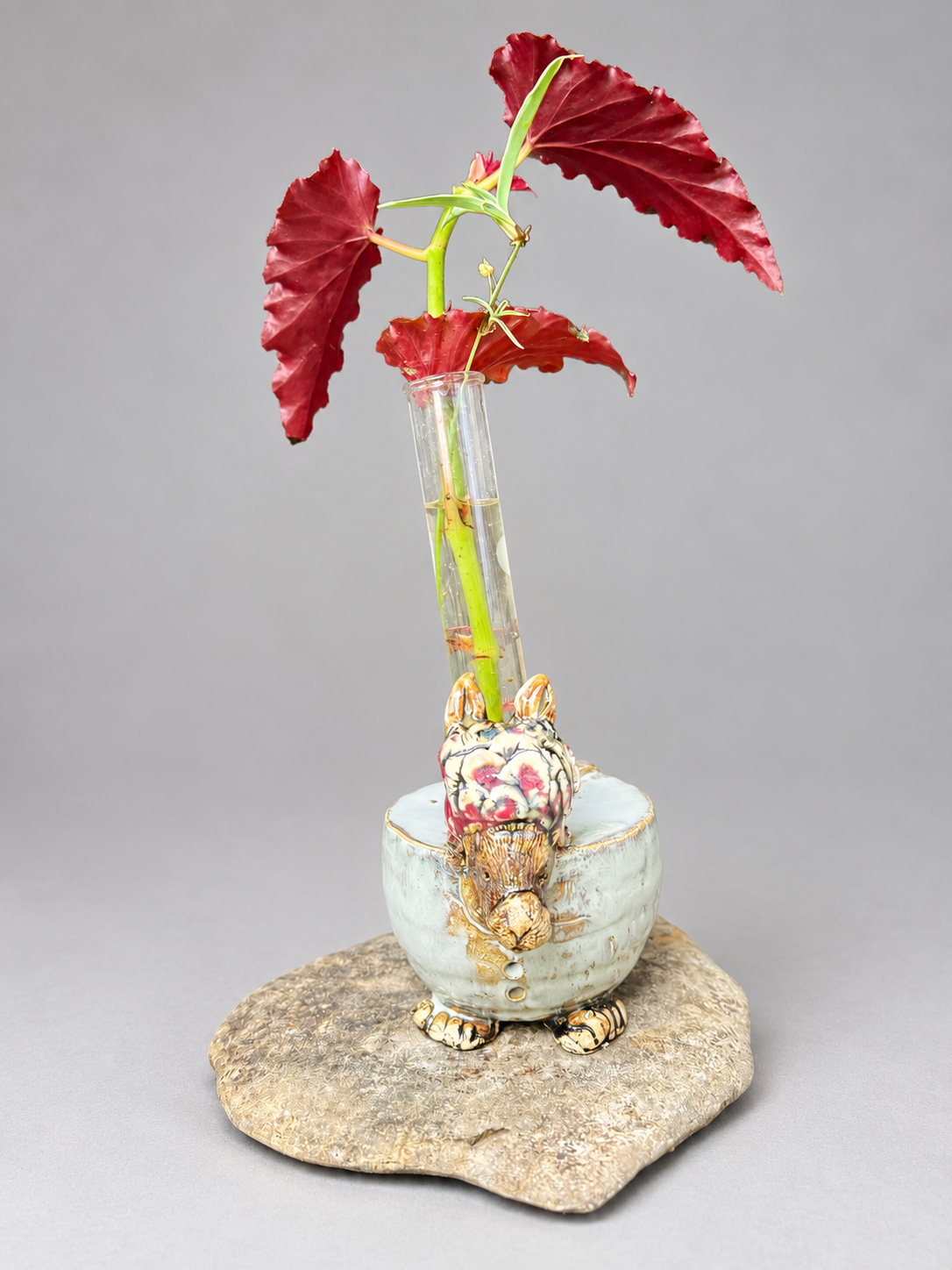 Rabbit-shaped ceramic propagation stand holding a glass tube with a red-leaved plant cutting